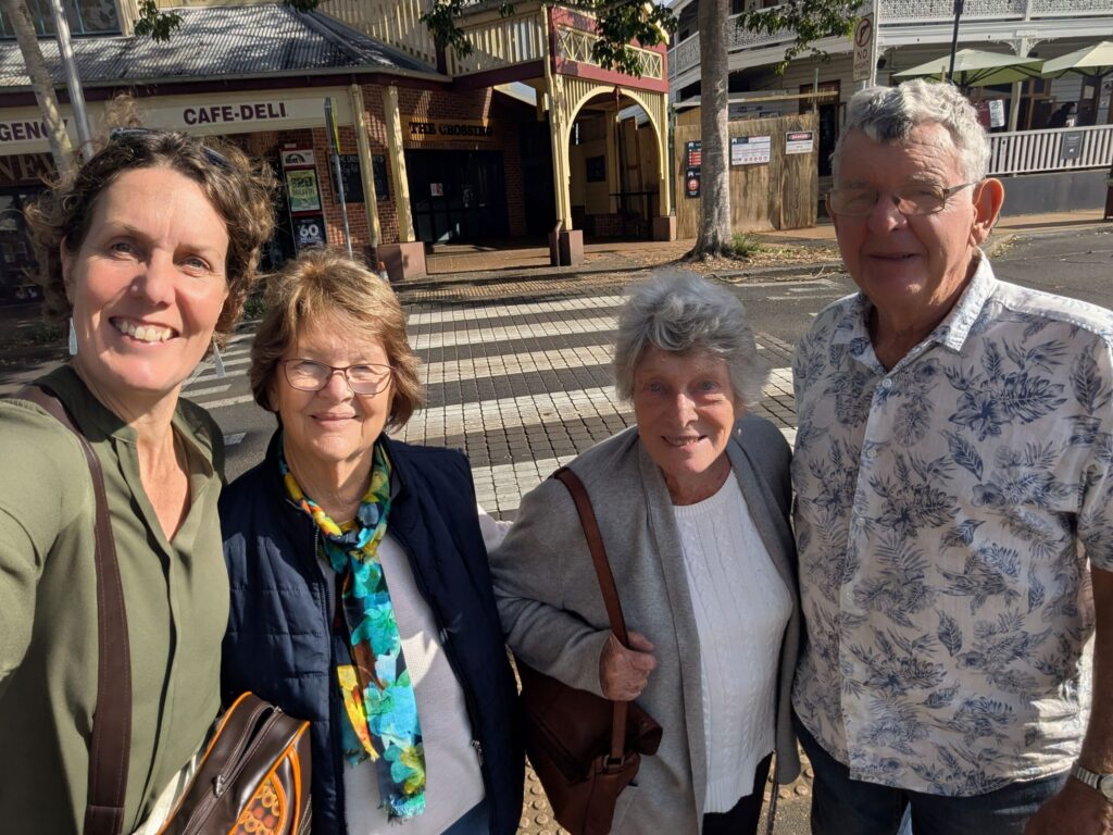 Four friends standing together on a street corner on a sunny day smiling at the camera