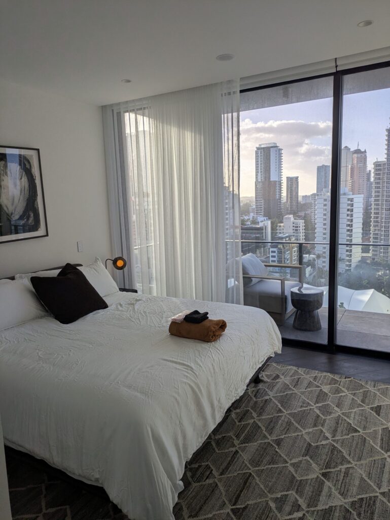 A bed in a hotel room, with a balcony and a view of a city skyline