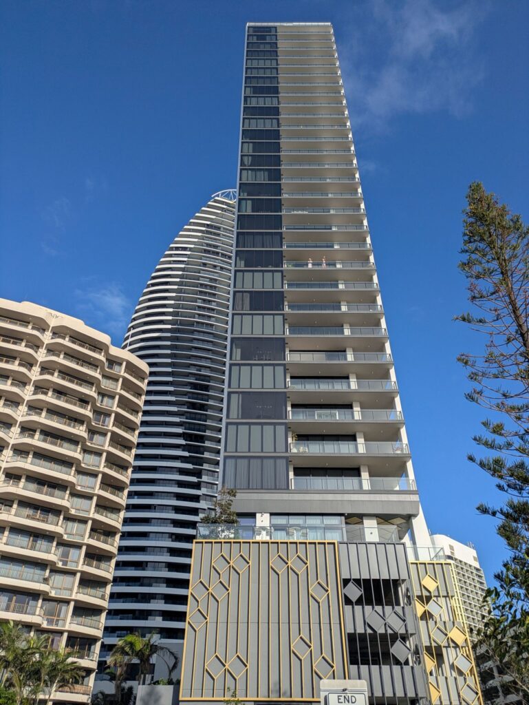 From the ground, looking up at a tall apartment building, with two women waving from a balcony halfway up