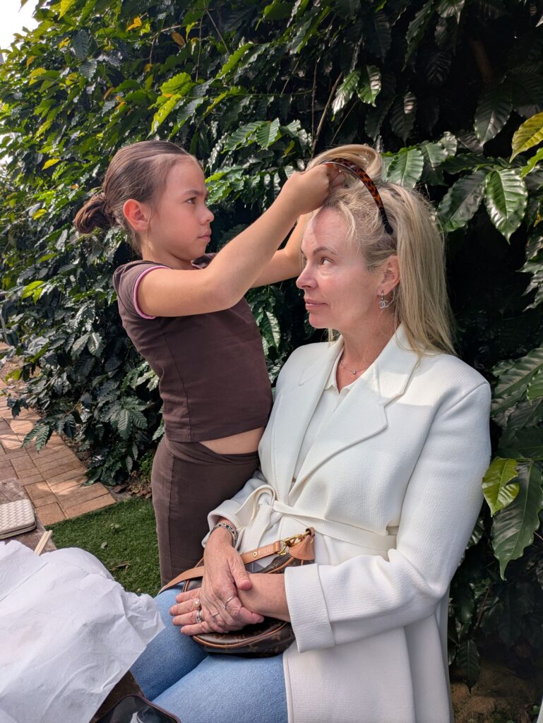 A girl standing in front of her seated mother, doing her hair